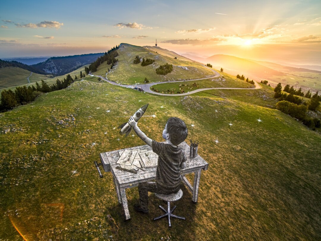 Fresque éphémère de Saype sur les pâturages du Chasseral : un enfant construisant une fusée, visible seulement depuis le bon angle